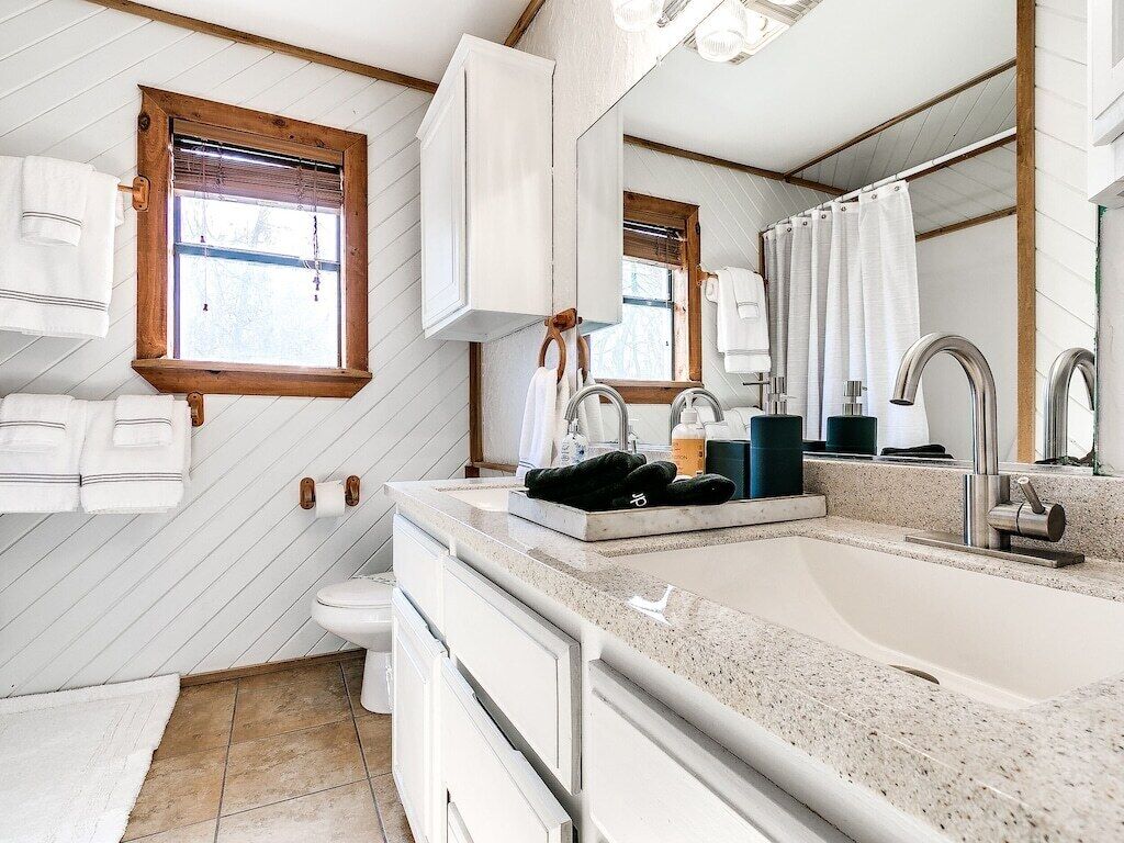 Un bagno moderno con uno specchio grande, un lavandino e un water. Asciugamani appesi al muro e una finestra con persiane.