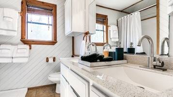 Un bagno moderno con uno specchio grande, un lavandino e un water. Asciugamani appesi al muro e una finestra con persiane.