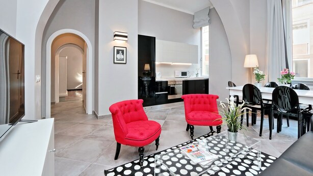 A modern living room with two red armchairs, a glass coffee table, and a dining area with black chairs.