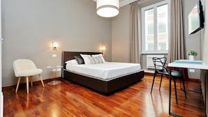 A modern bedroom with a large bed, bedside lamps, a desk with a chair, and a TV on the wall. - Monti Apartments - M8 (Rome)
