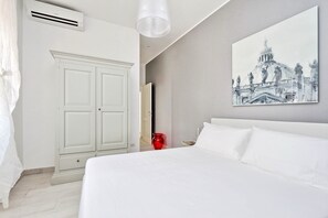 A bedroom with a large bed, a white wardrobe, a red vase, and a painting of a building on the wall. - Monti Apartments - M16 (Rome)