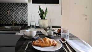 A breakfast setting with croissants, coffee, and water on a table, a plant, and a TV in the background. - Il mulino di Trastevere - G2 (Rome)