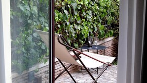 Un patio con una silla plegable blanca, una mesita y una copa de vino.