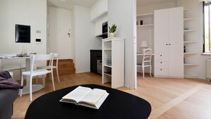 Una habitación moderna y bien iluminada con zona de comedor, una mesa negra con un libro abierto, muebles blancos y un amplio armario blanco.