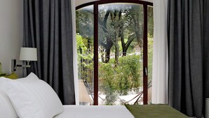 Habitación de hotel con cama, lámpara y vista a la vegetación a través de un ventanal.