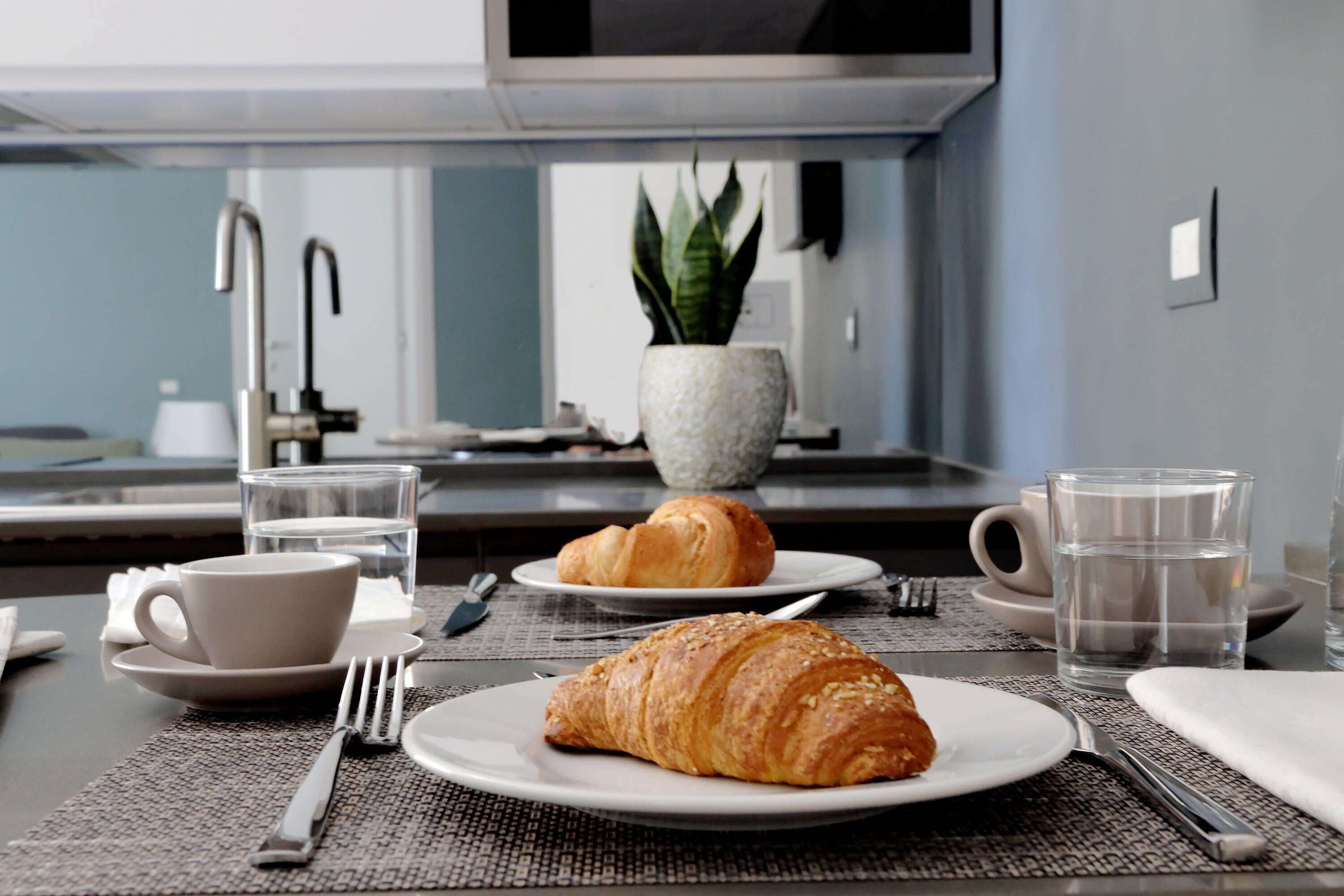 Ein Frühstückstisch mit Croissants, einer Tasse und einem Glas Wasser.