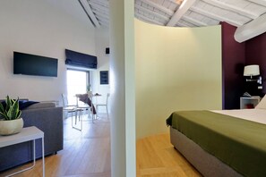 Una habitación de hotel moderna con una cama, un sofá, un televisor y un rincón de comedor al fondo.