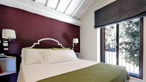 A bedroom with a large bed, white bedding, a green throw, and a view of trees through a window.