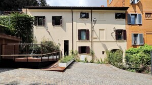 A cobblestone courtyard with a building featuring multiple windows and a small garden area.