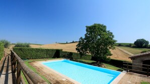 Una piscina rectangular con una cubierta de madera y un borde de piedra, rodeada por una valla de madera y un seto.