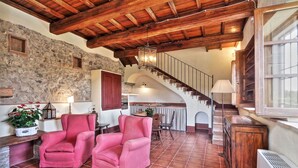 Un interior rústico con paredes de piedra, vigas de madera, una escalera y una zona de comedor con mesa y sillas.