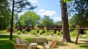 A wooden deck with Adirondack chairs and a table, surrounded by lush greenery and trees.