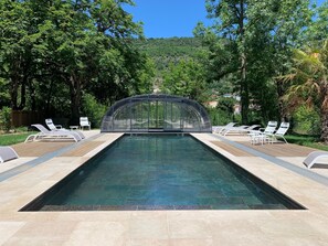 Une piscine dotée d’une enceinte en verre, entourée de chaises longues et d’une terrasse en bois.