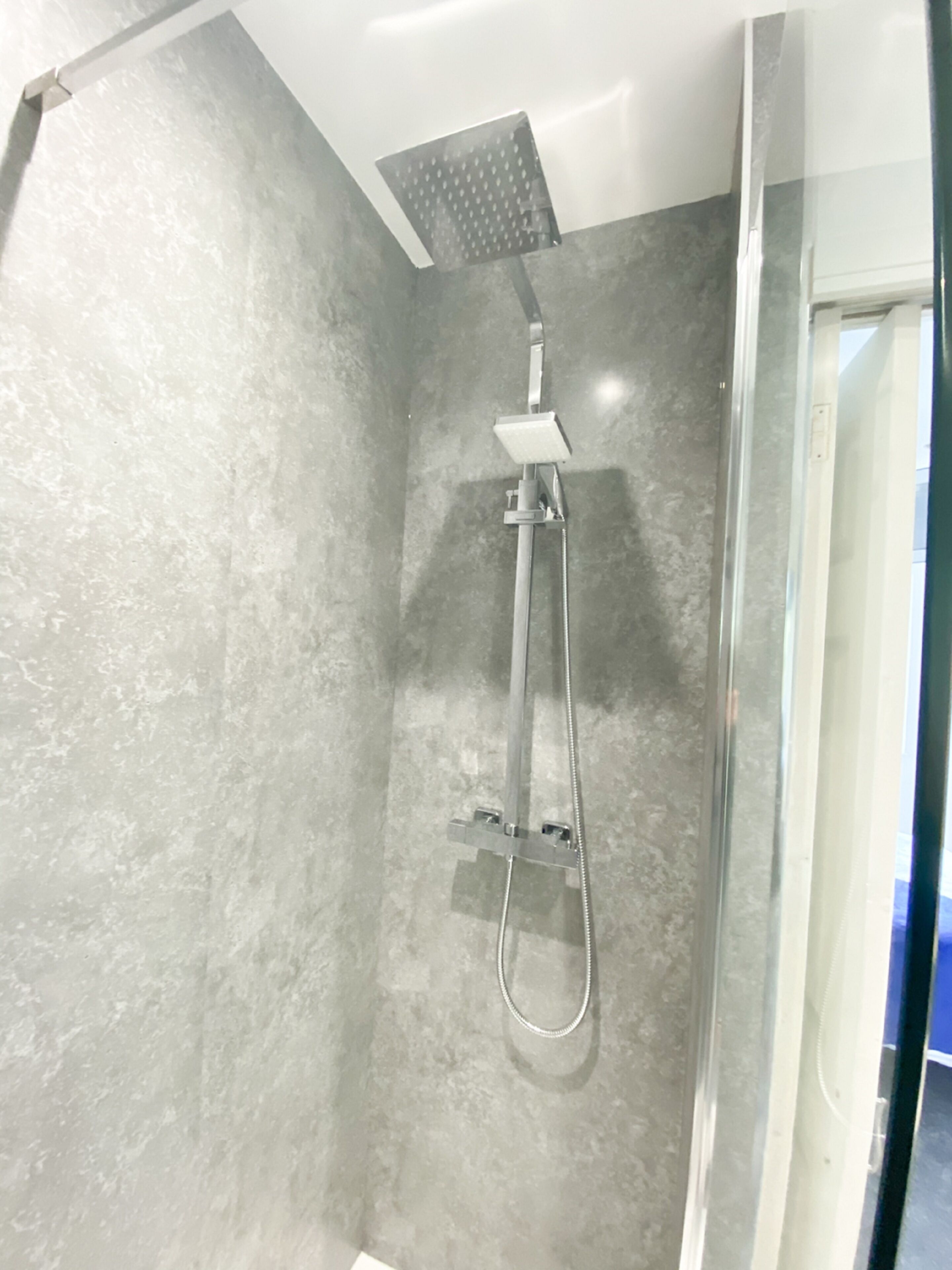 Une douche équipée d’un pommeau de douche à main et d’un panneau de commande fixé au mur.