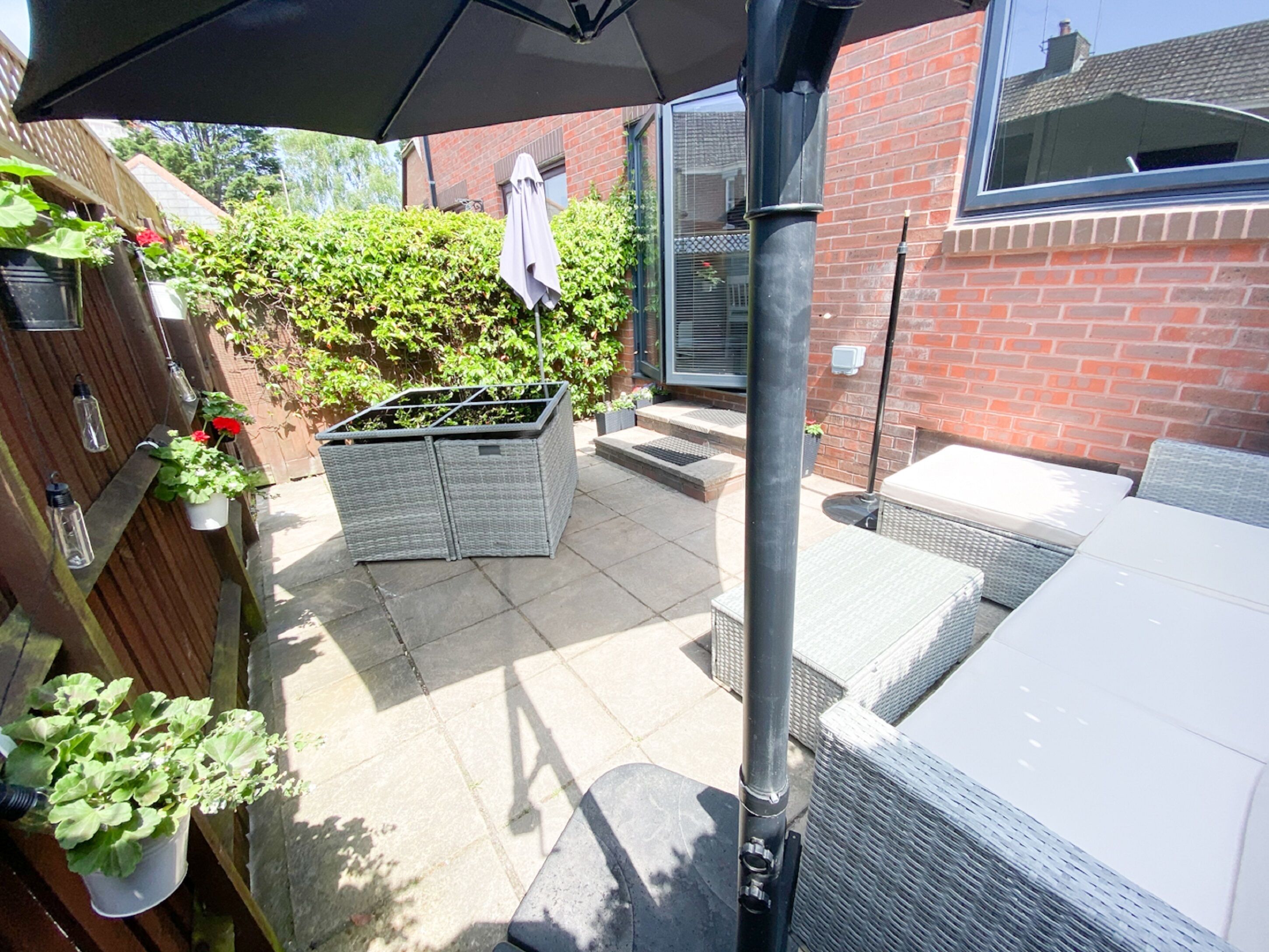 A patio area with wicker furniture, a black umbrella, and potted plants.