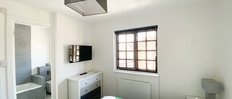 A bedroom with a bed, a dresser, a television, a window, and a bathroom.