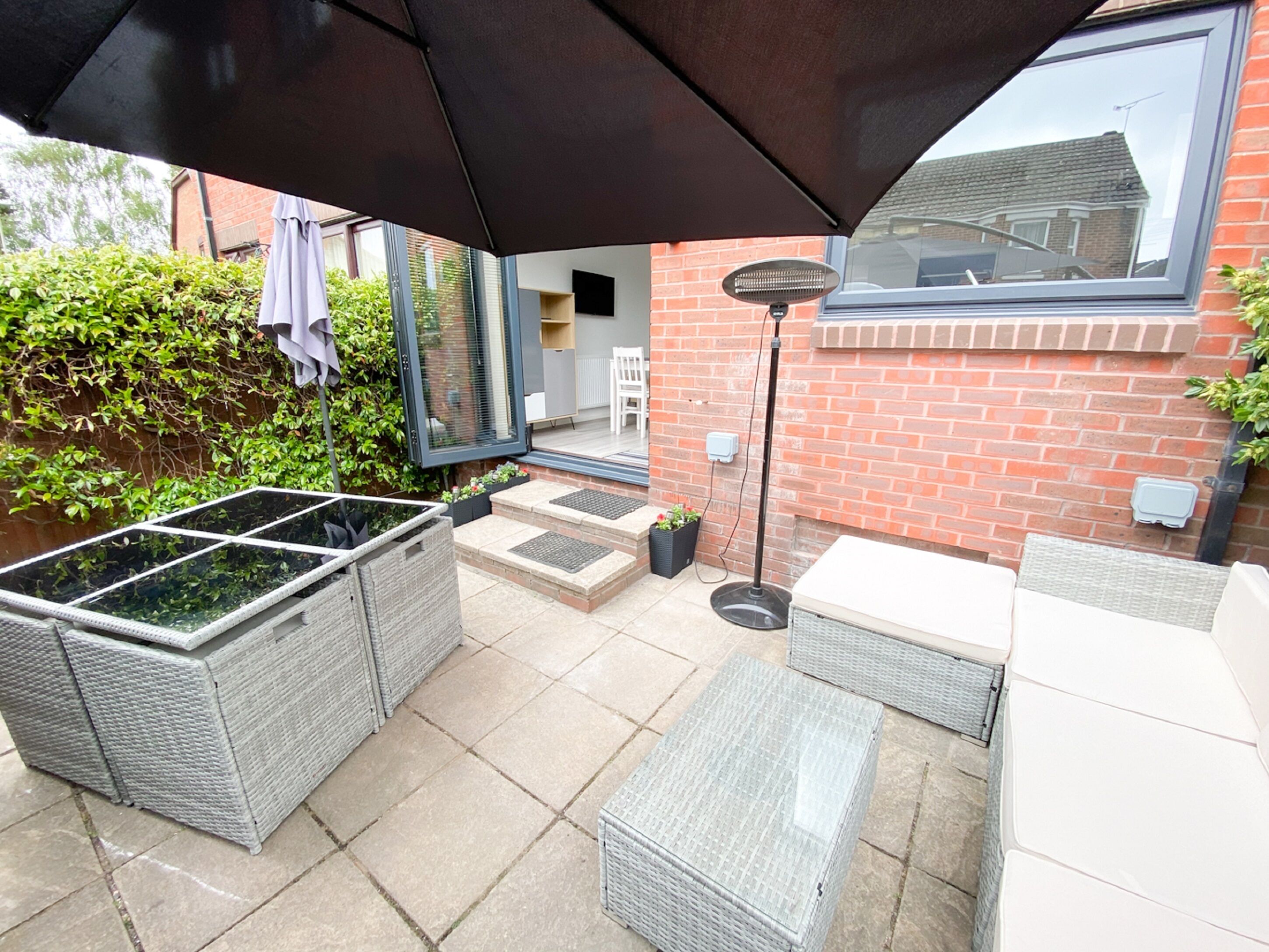 An outdoor patio area with wicker furniture, a black umbrella, and a brick wall.