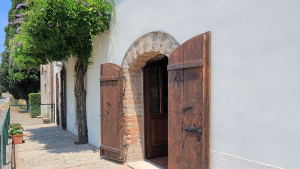 A narrow cobblestone pathway leading to a rustic building with wooden shutters and a stone archway.