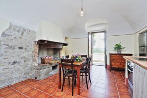 A dining area with a brick fireplace, wooden table, chairs, and a potted plant.