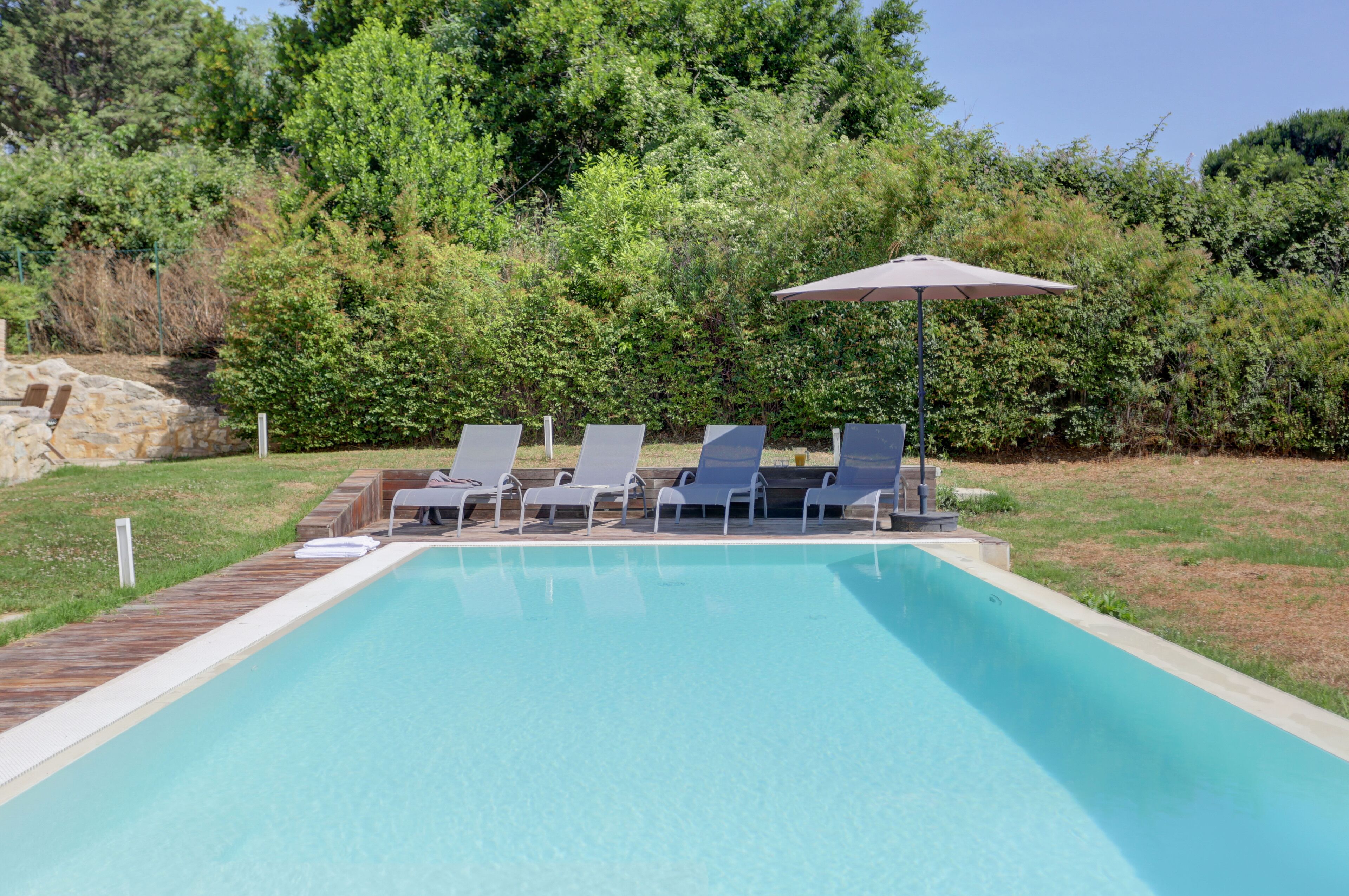 A rectangular swimming pool with a wooden deck and lounge chairs.