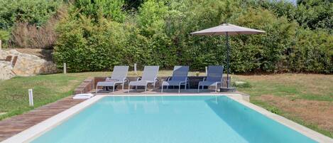A rectangular swimming pool with a wooden deck and lounge chairs.