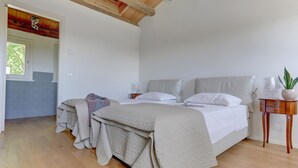 Une chambre avec deux lits, un plancher en bois, une fenêtre et une porte donnant sur une autre pièce.