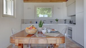 Une cuisine moderne avec des meubles blancs, une table à manger en bois et une fenêtre donnant sur des arbres.