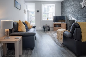 Uma sala de estar moderna com um sofá de couro preto, uma mesa de centro de madeira e uma TV sobre um móvel de madeira.