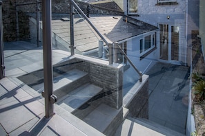 Escadaria moderna ao ar livre com guarda-corpos de vidro, que dá acesso a um terraço.