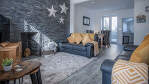 Un salon moderne avec un mur en briques sombres, un canapé en cuir noir et une table basse en bois.