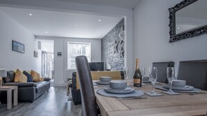 Un espace de repas moderne avec une table en bois dressée pour quatre personnes, un canapé en cuir noir et une grande œuvre d’art abstraite accrochée au mur.