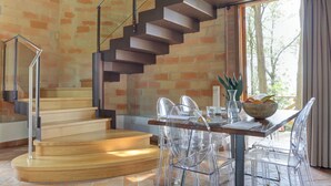 A modern interior with a wooden staircase, clear chairs, and a dining table with a bowl of fruit.