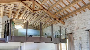 A spacious loft with exposed wooden beams, a glass balcony, and a stone wall.