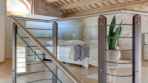 A bedroom with a glass door, a bed, a potted plant, and a staircase.