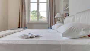 Ein ordentlich bezogenes Bett mit einem Buch, einem Fenster mit Vorhängen und einer Nachttischlampe.