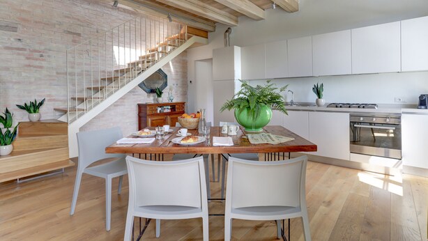 A modern kitchen with white cabinets, a stainless steel stove, and a wooden dining table with chairs.