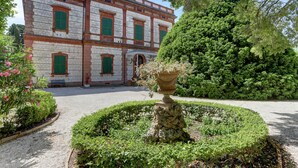 A historic building with a symmetrical facade, a central courtyard with a fountain, and well-maintained hedges.