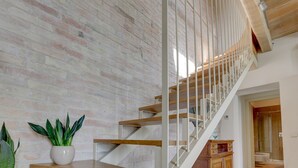A staircase with wooden steps and white railings, leading to a room with a brick wall and a potted plant.
