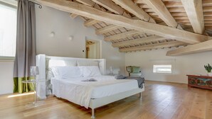 A bedroom with a wooden ceiling, a bed, a bedside table, a lamp, and a window with curtains.