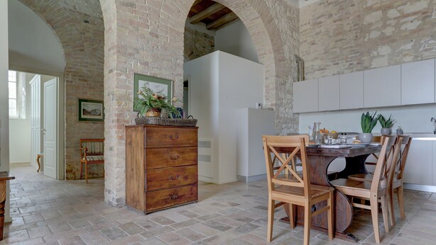 Una cocina amplia con una pared de ladrillo rústica, una mesa de madera con sillas y un armario blanco.