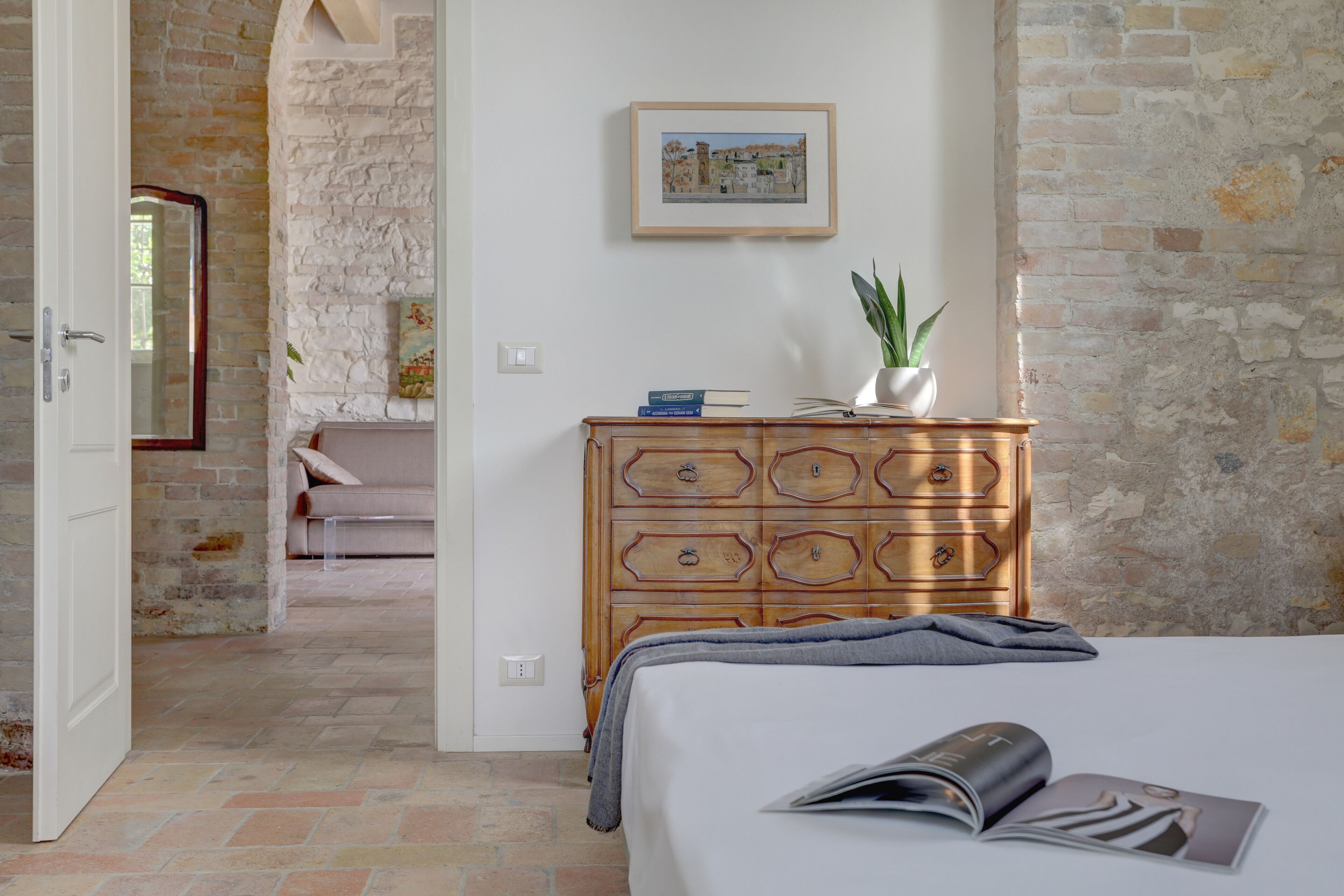 Ein Schlafzimmer mit einem Bett, einer hölzernen Kommode, einem gerahmten Bild an der Wand und einem Blumentopf.