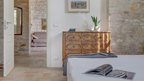 Un dormitorio con una cama, un aparador de madera, un cuadro enmarcado en la pared y una planta en maceta.