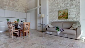 Una cocina moderna con armarios blancos, una zona de comedor con sillas de madera, un sofá y una mesa de centro.
