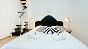 Une chambre à coucher avec un lit, deux lampes de chevet, une tête de lit, une décoration murale représentant une tête de cerf, un escalier avec des marches noires et blanches, et deux serviettes sur le lit.