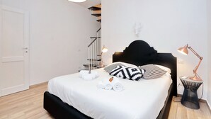 Une chambre moderne avec un lit, deux lampes de chevet, une tête de lit noire, une porte blanche et un escalier en arrière-plan.