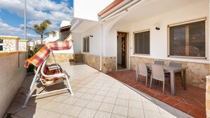 Un patio con una mesa y sillas, una zona de estar cubierta y una pared de piedra.