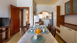 Un comedor con una mesa lista para cuatro personas, un televisor sobre un mueble bajo y armarios de madera.