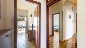 Un pasillo con un marco de puerta de madera, suelo de baldosas y vista a un comedor con una mesa y sillas.