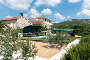 Uma vila de dois andares com piscina, área de estar externa e vista para as colinas ao redor.