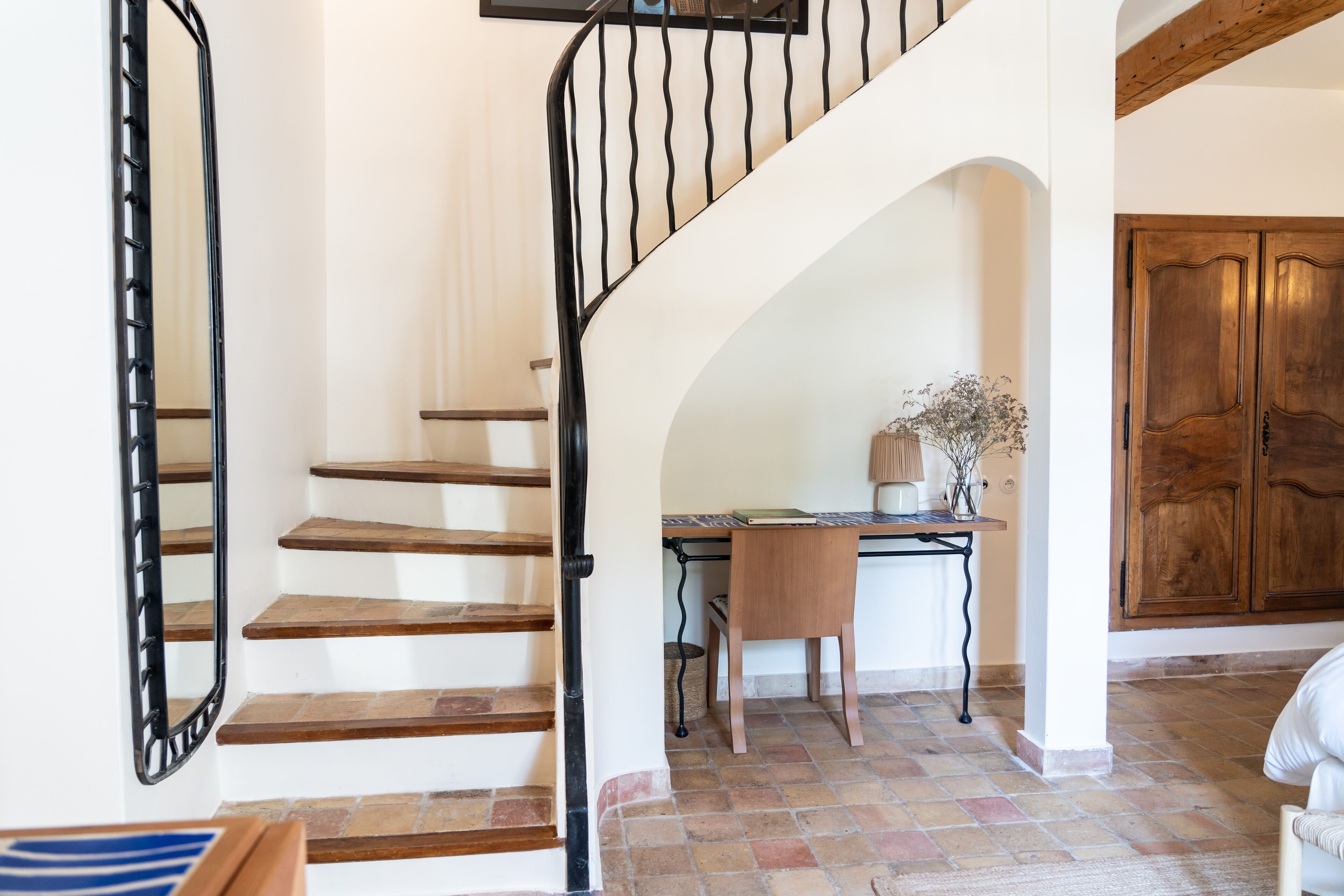 A staircase with wooden steps and black metal railings, leading to an archway with a desk and chair.